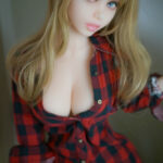 Pearl 150cm Piper Doll G Cup with long blond hair in a red and black checked shirt standing indoors