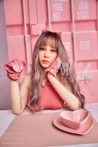 Aika 158cm D-Cup WM Doll Head silicone #70 poses with pink clothing and accessories, sitting at a table with a heart-shaped dish.