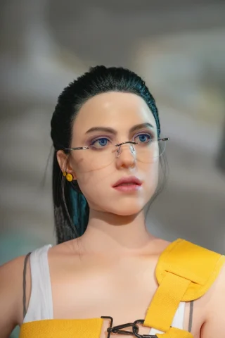 Mama Malingen doll features long black hair, glasses, and a yellow harness over a white tank top, with a neutral expression.