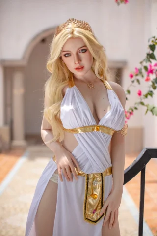 Starpery 172cm F-Cup Rozanne, wearing a white gown with gold accents, poses elegantly outdoors with flowers in the background.