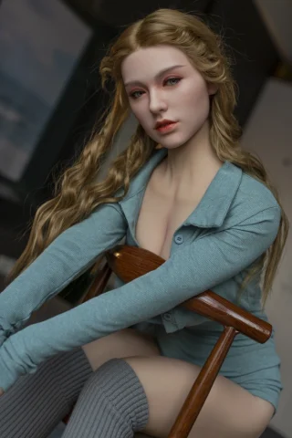 Tiffany 167cm E cup doll with long blonde hair, wearing a teal top and gray thigh-high socks, seated on a wooden chair.