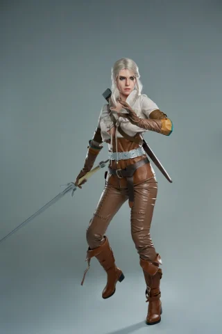 Ciri doll in a fighting pose, wearing a brown leather outfit with a sword and a hooded jacket.
