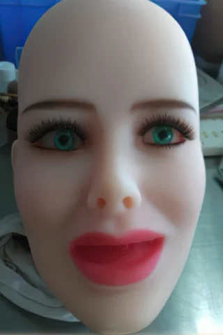 Doll head with blue eyes, long eyelashes, and a neutral expression, featuring light skin and red lips.