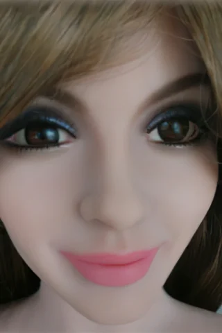 Doll face with brown eyes, long brown hair, and soft pink lips, featuring detailed makeup.