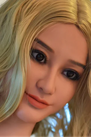 Doll with long blonde hair, featuring large brown eyes and a soft smile, set against a light background.