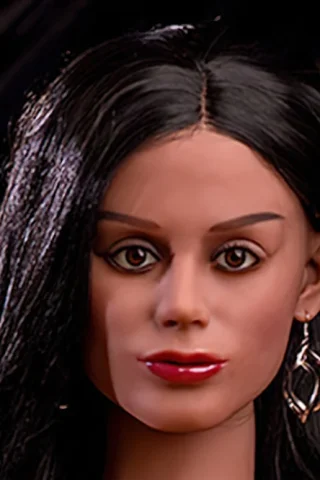 Doll 160cm with long black hair, wearing silver earrings and a subtle makeup look, seated against a dark background.
