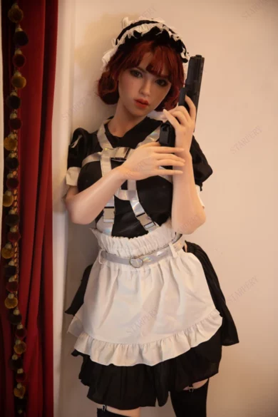 Sex doll in maid outfit with red tassels holds toy gun against wall