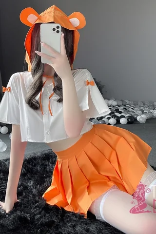 Playful Hamster outfit featuring a white cropped top with orange accents and an orange pleated skirt, set against a soft black rug.