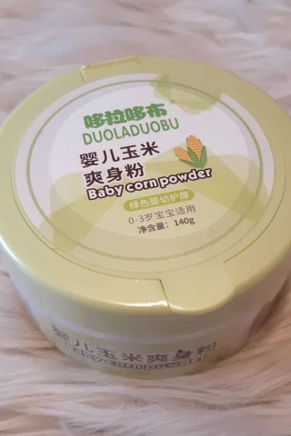 Baby Corn Powder container with a light green lid, featuring corn graphics and text in Chinese, placed on a fluffy white surface.