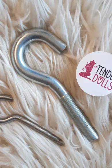 Two metal hooks from the Hook Kit for Storage M16 on a fluffy white surface next to a Tender Dolls sticker, suggesting a link to love dolls.