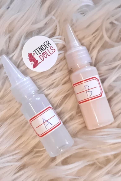 Two small bottles labeled A and B on a plush surface with a round Tender Dolls sticker beside them, part of a TPE Sex Doll Glue Kit.