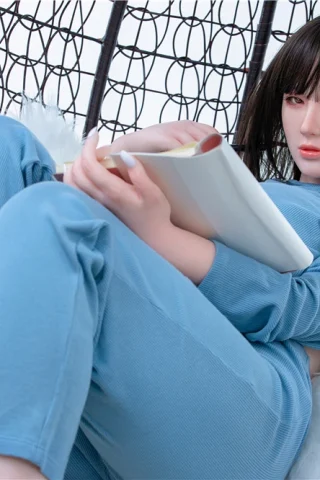 S1 Miya 160cm Irontech sex doll seated in a hanging chair, wearing a light blue outfit and holding a book.