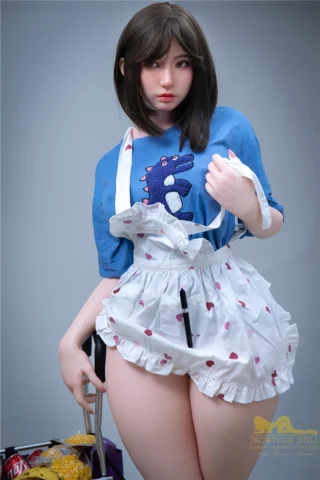 Suki S20 164cm E Cup Irontech doll wearing a blue shirt and white apron with a heart pattern, holding a pen.