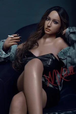 A person with long hair in a dark outfit and denim jacket sits cross-legged, holding a cigarette, resembling the XNX Taylor 164cm X12 Doll.