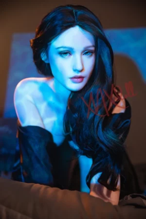 A woman with long dark hair softly illuminated by blue light, reminiscent of the XNX Cara Cara X7 149cm Doll, gazes at the camera dressed in a black garment