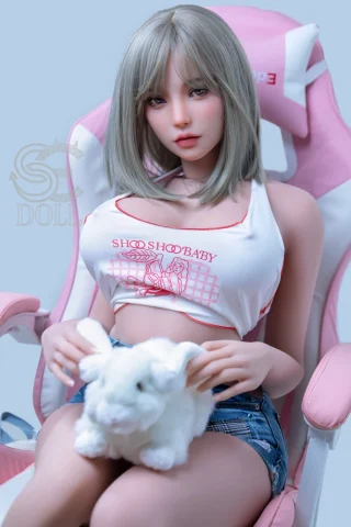 Akina 157cm H Cup #088 SE Doll sitting in a pink gaming chair, wearing a cropped white top and denim shorts, holding a white plush bunny.