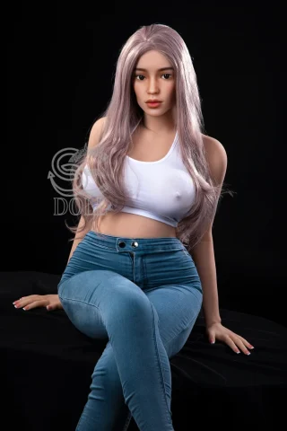 Beth 161cm G Cup doll seated in a black setting, wearing a white crop top and blue skinny jeans.