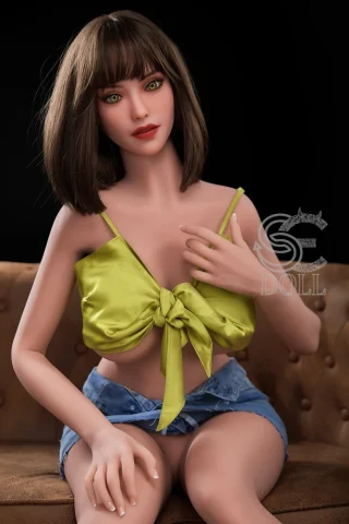 Grace 157cm H Cup #020 SE Doll sits on a couch, wearing a green tied top and denim shorts, with brown hair and green eyes.