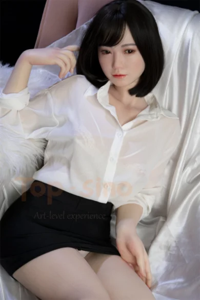 A love doll with short black hair wearing a white blouse and black skirt sits on a sofa in a relaxed pose.