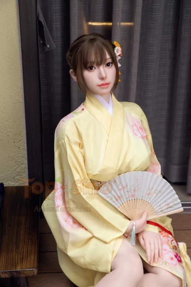 Figure wearing T28 Minai T168 Top Sino in vibrant yellow sits indoors holding a folding fan