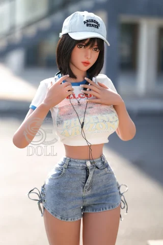 SED233 161cm Stella wearing a white crop top and denim shorts, with a cap and headphones, standing outdoors.
