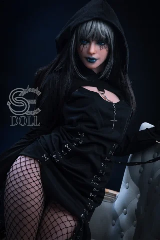 Heloise 166cm B Cup wearing a black hooded outfit with fishnet stockings, posing on a white chair against a dark background.