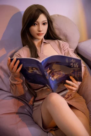 A long-haired figure resembling a T27 Mitao 164cm love doll sits on a cushioned chair reading a magazine with a calm expression.