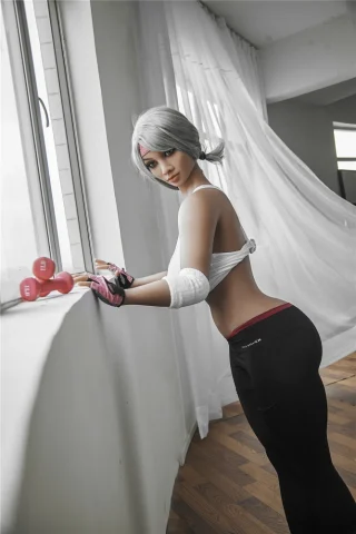 Ayumi 158cm I Cup Irontech TPE poses by a window, wearing a white crop top and black leggings, with dumbbells nearby.
