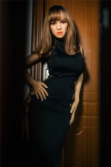 Elegant sex doll wearing a black dress stands confidently by a wooden door, exuding sophistication and allure.