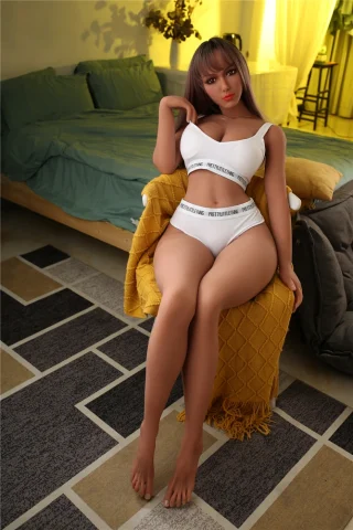 Plus Scarlet 164cm E Cup Irontech TPE doll sitting on a couch, wearing white lingerie, with a yellow throw blanket nearby.