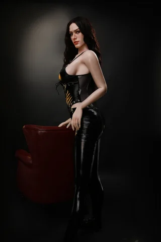 Nieve 176cm F Cup Starpery stands in a black latex outfit next to a red chair, with long dark hair and a side pose.
