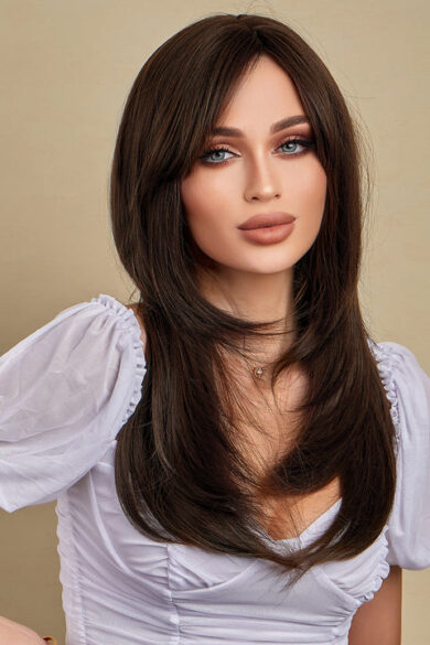 A woman wearing a wavy wig and white blouse poses against a beige background.