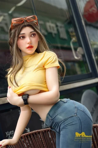 S40 159cm E Cup Irontech doll wearing a yellow crop top and blue jeans, posing outdoors with sunglasses on her head.