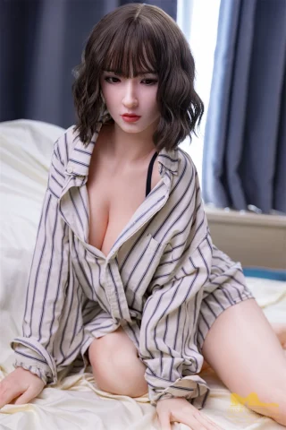 S7 165cm F Cup Irontech doll wearing a striped oversized shirt, kneeling on a bed with a soft gray backdrop.