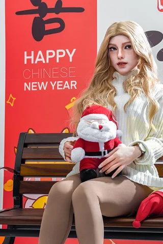 S31 163cm C Cup Irontech doll wearing a white sweater and beige tights, sitting on a bench with holiday decorations.