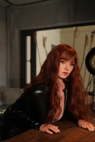 Natalia ROS 165cm D Cup in a black latex outfit, leaning over a wooden table with long wavy red hair and striking green eyes.