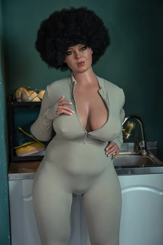 Ursula ROS 161cm H Cup stands in a fitted beige jumpsuit, showcasing her curves and an afro hairstyle.
