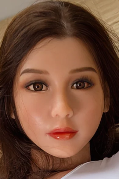 Close-up of #70 WM/YL/OR silicone doll head with long brown hair, detailed facial features, and bright eyes on a bed