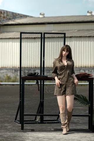 170cm S23 Catlin RealLady stands against a mesh backdrop, wearing a brown shirt dress and knee-high beige boots.