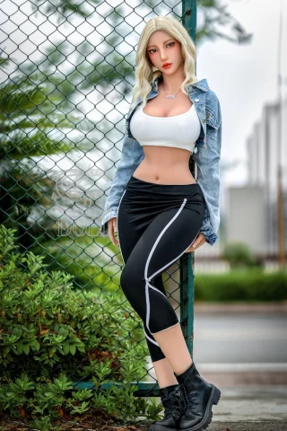 SED313 161cm Makoto stands against a green fence, wearing a white crop top, denim jacket, black leggings, and black boots.