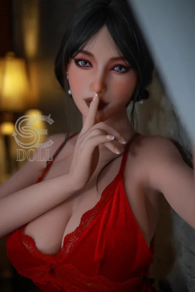 A figure in a red outfit poses indoors with a finger to her lips, softly lit by a lamp, similar to the Felicia.E 157cm H Cup SE Doll.