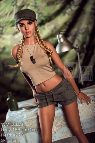 Amber 166cm C Cup doll wearing a beige crop top and green shorts, posed beside a map and a desk lamp.