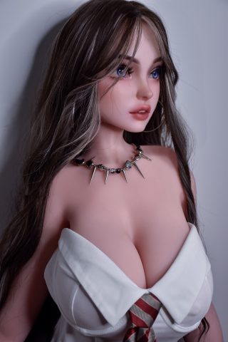 A lifelike doll with long, wavy hair, wearing a white shirt with an open collar and a spiked necklace, poses against a plain background.