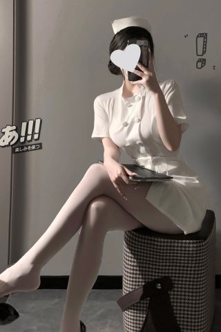 A woman in a short, fitted white secretary outfit poses in front of a mirror, holding a clipboard, with one leg crossed over the other.