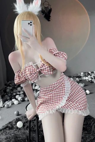 A figure in a red and white checkered tube dress with ruffled edges, posing playfully with bunny ears in a softly lit room.