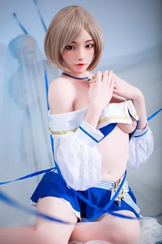 A doll with short blonde hair poses in a blue and white outfit, featuring a cropped top and a short skirt, against a soft backdrop.