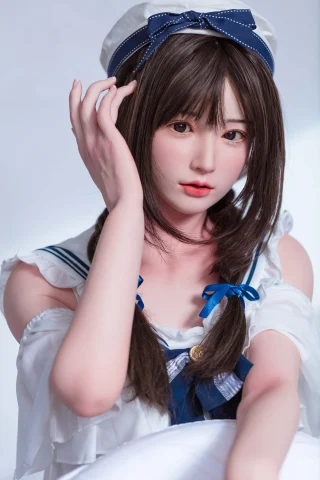 A young woman with long, dark hair styled in braids, wearing a sailor-themed outfit with blue accents, poses gently with one hand touching her hair.