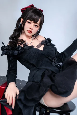A young woman in a black dress with floral embellishments lounges on a stool, wearing a red bow in her hair and a pearl necklace.