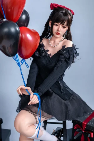 A figure in a black off-shoulder dress with ruffled details sits on a stool, holding red and black balloons, with a red bow in her hair.