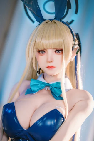 A doll with long blonde hair and bunny ears wears a shiny blue outfit with a bow tie, featuring large expressive eyes and a soft expression.